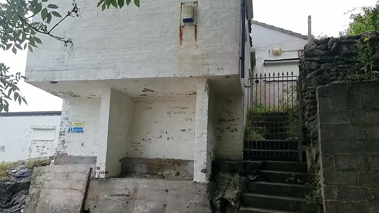 Camera angles down at derelict beach house, where weathered concrete stairs surrender to the tide and grey skies amplify desolation. Ideal for mystery or urban decay narratives