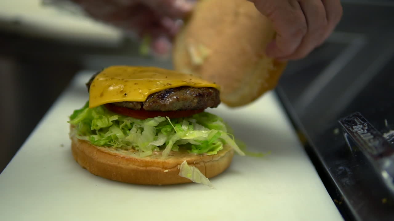 Un lavoratore di fast food mette il panino sopra il cheeseburger, primo piano al rallentatore.