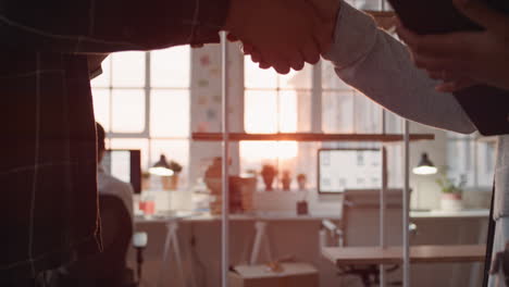 young-asian-businessman-working-late-software-developer-meeting-client-shaking-hands-collaborating-with-intern-on-designing-mobile-application-in-office-at-sunset