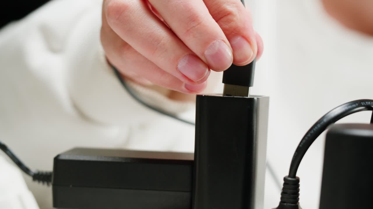 White power strip with many various of cords and cables in close-up. An extension cord with many power sockets. Adapter with phone, headphones, usb connectors.Tangled wires on table. Trying to untangle many messy cables.