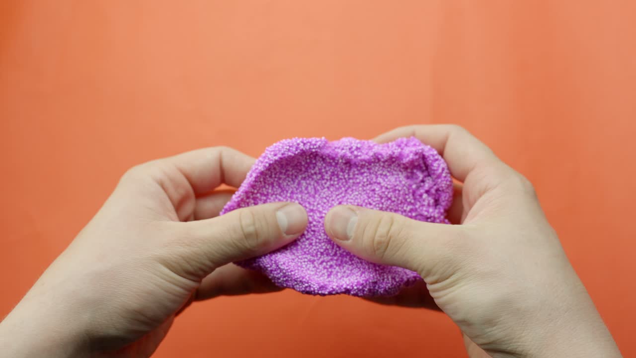 Close-up of pink Floam slime being pulled and stretched in front of a vibrant red backdrop.