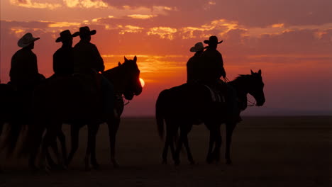 cowboys riding horses at sunset