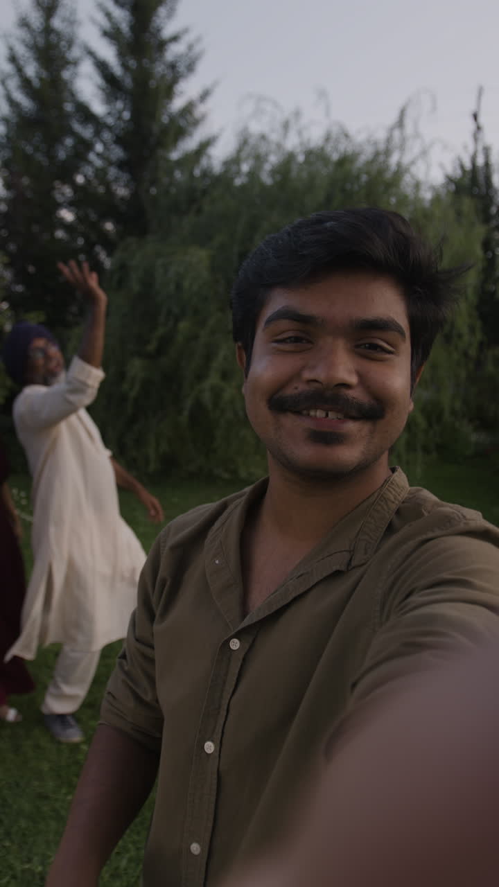 Smiling Young Man Taking a Selfie at an Outdoor Celebration with Friends and Family