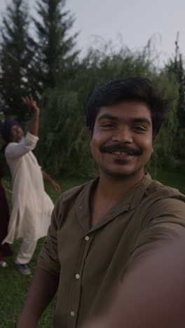 smiling young man taking a selfie at an outdoor celebration with friends and family