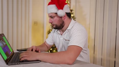 focused businessman entrepreneur wearing santa hat working on a laptop during the christmas holiday in his house home office with decorated xmas tree in the background