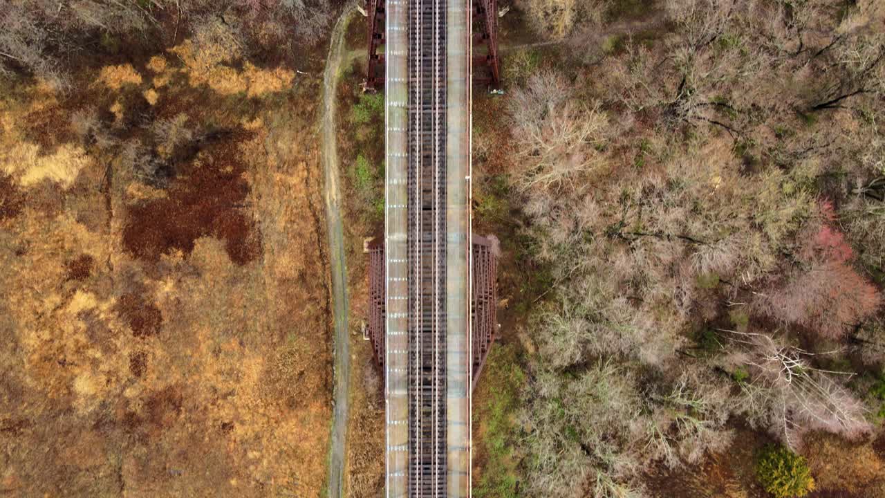 imágenes de video de drones aéreos, de arriba hacia abajo, de un viaducto de un puente de tren que corre sobre un valle y un arroyo en las montañas appalachain a principios de la primavera en un día de nubes