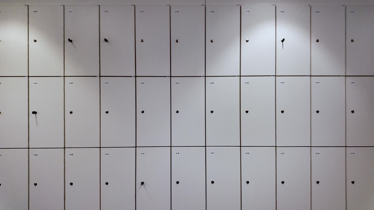 Close up of a wall of numbered office lockers, some showing keys and keyholes, providing secure storage for employees