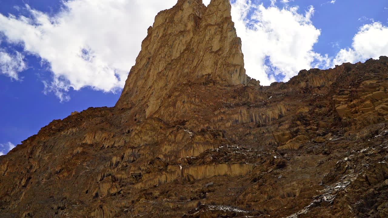 tiro inclinado hacia abajo desde una extraña formación rocosa gigante contra el cielo azul con una nube blanca sobre la montaña