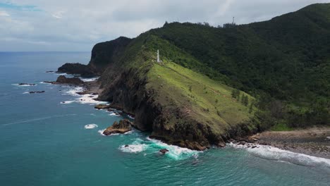 a stunning wide shot showcases a lighthouse standing tall on a small coastal mountain, with the shoreline and ocean stretching endlessly beyond.