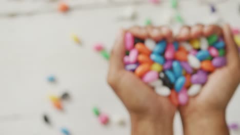 Video-of-overhead-view-of-biracial-man-holding-multi-coloured-sweets-over-white-rustic-background