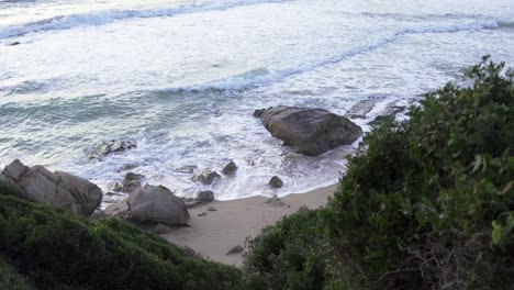 Beach-with-rocks-and-strong-waves,-clip-camera-in-hand,-taken-among-vegetation