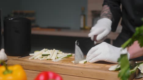 Fresh-zucchini-being-sliced-on-a-wooden-board-by-young-professional-male-chef-in-an-elegant-black-shirt-with-tattoos