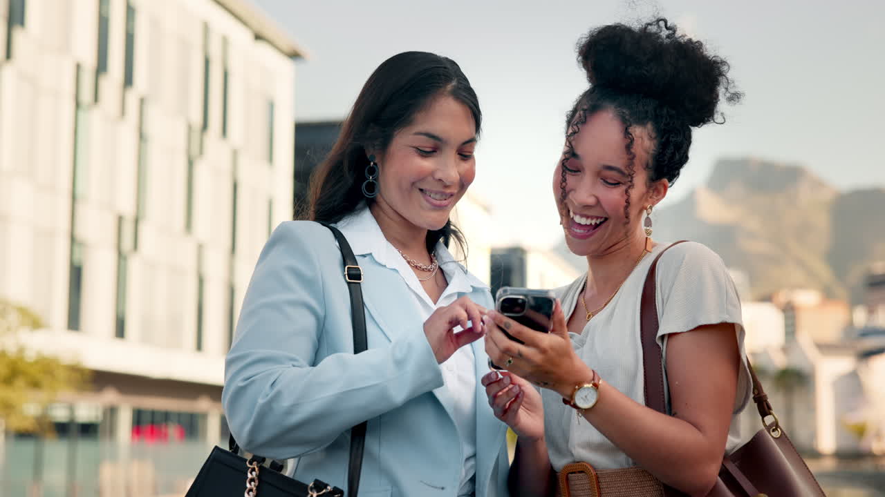 dos mujeres de negocios riendo mientras miran un teléfono inteligente