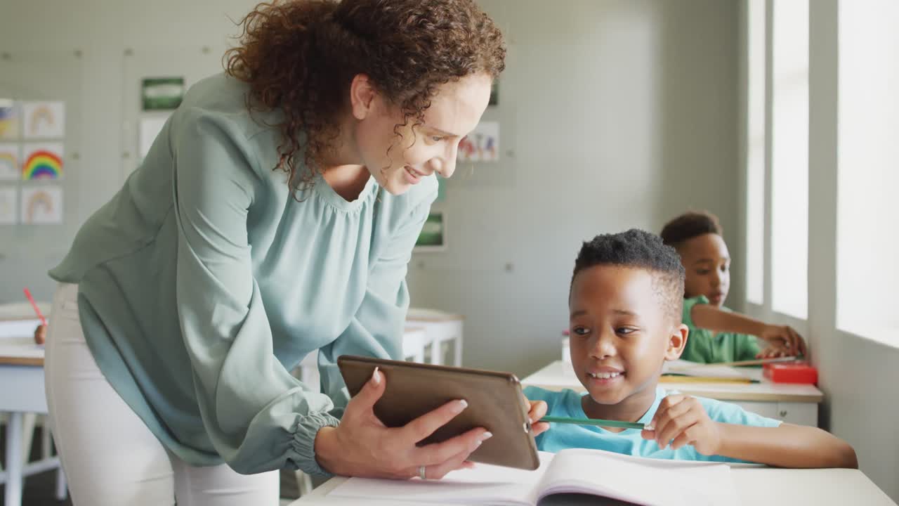 video de una feliz maestra caucásica explicando la lección en una tableta a un niño afroamericano