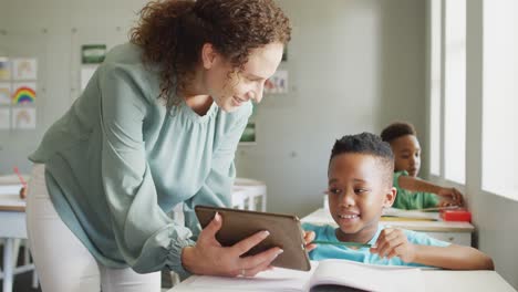 Video-of-happy-caucasian-female-teacher-explaining-lesson-on-tablet-to-african-american-boy