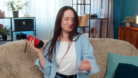 happy woman dancing on sofa with wireless speaker laughing enjoying music raising hands rock gesture