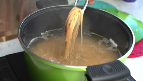 hot boiling water with spaghetti cooking, steam rising, checking if the pasta is cooked