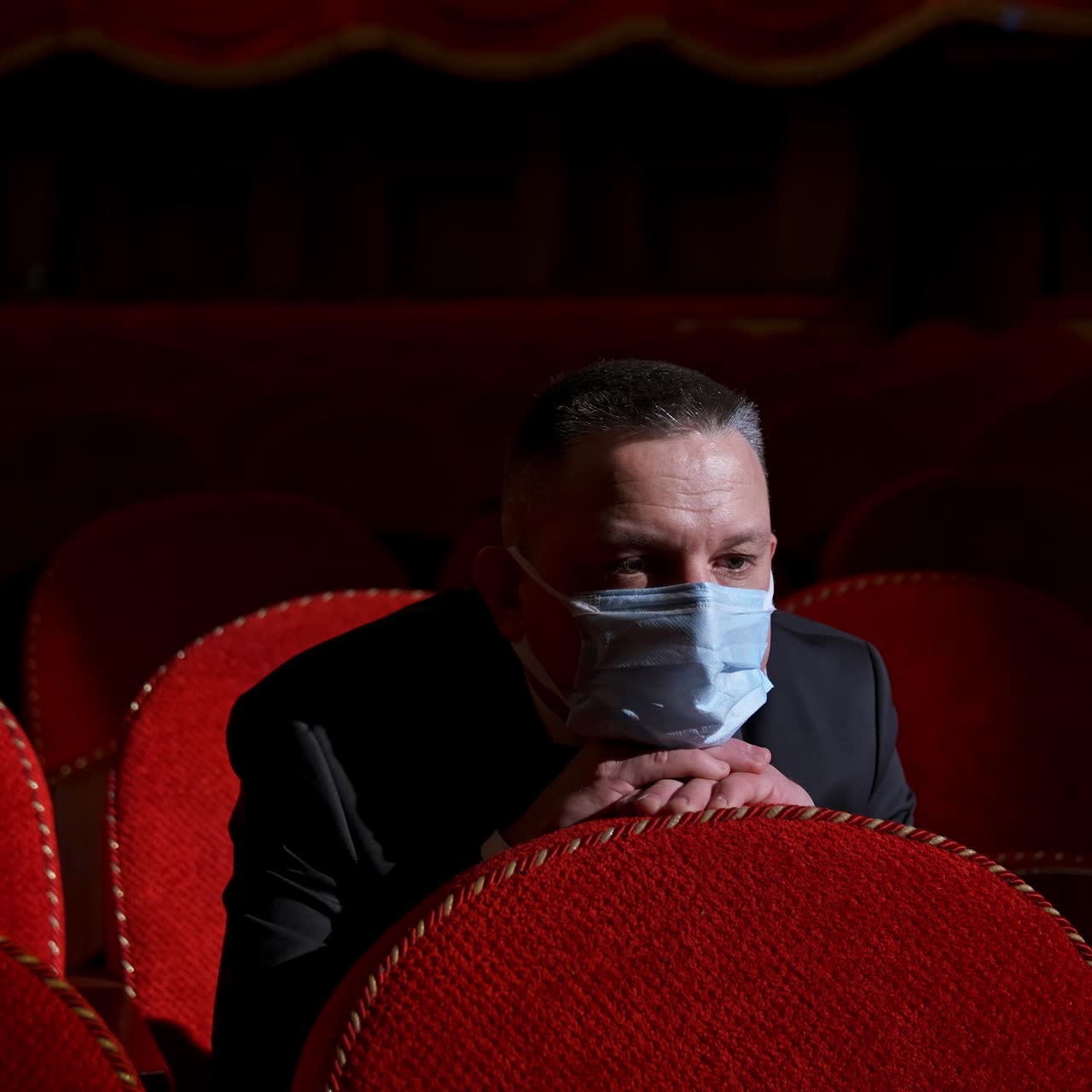Man sits in the middle of empty theater hall with red velvet chairs. Actor is alone in theater. Lockdown and pandemic concept