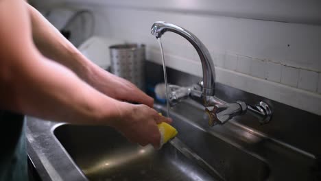 caucasian male washing cutlery with yellow sponge in silver kitchen sink