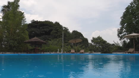 Blick-Auf-Den-Wasserspiegel-Des-Swimmingpools-Mit-Leichten-Tropischen-Regentropfen,-Wolke