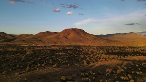 aerial view, drone flying towards a butte in the desert at sunset, brush and plants in foreground, light blue skies, golden hour in arizona