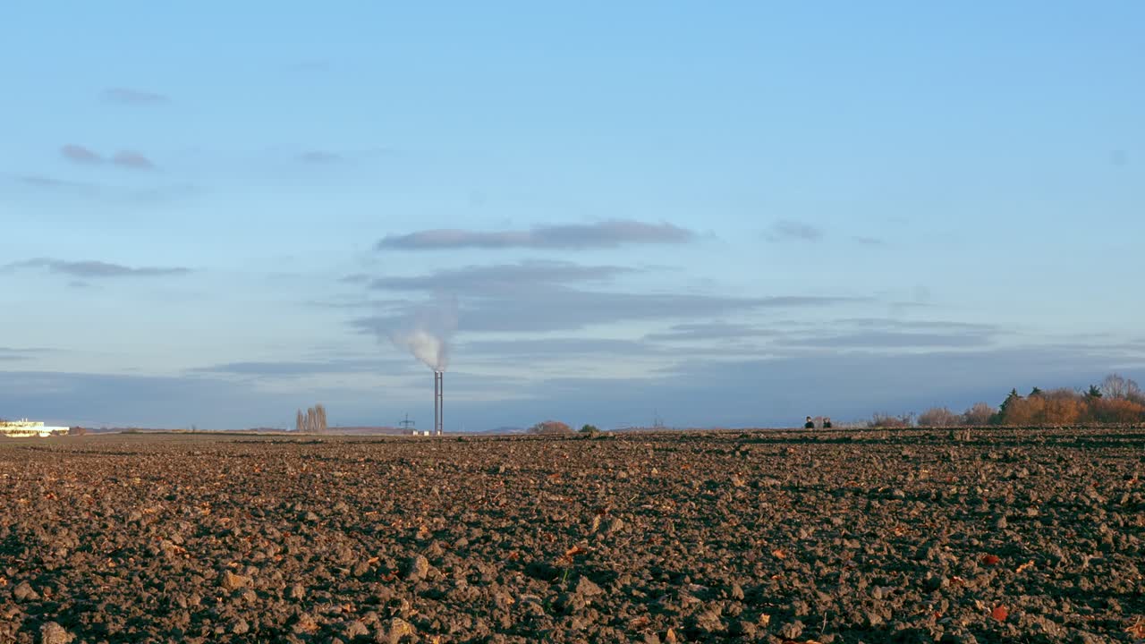 수평선 위를 걷는 사람들과 일하는 굴뚝이 있는 빈 갈색 들판