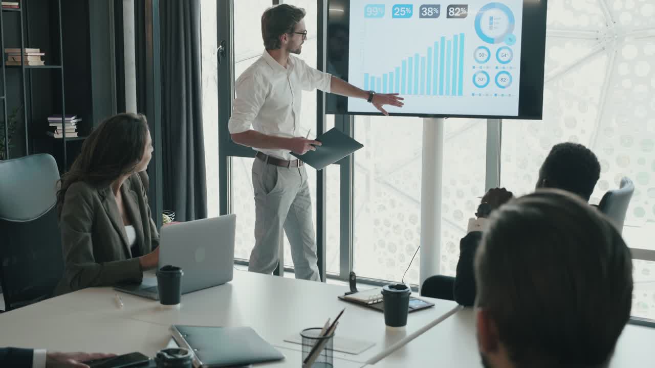 joven trabajador barbudo de pie junto a la tabla de vidrio con diferentes notas, tocando papeles multicolores. mirando serio y confiado. vista de cerca de apuesto hombre de negocios, de pie en la oficina interior