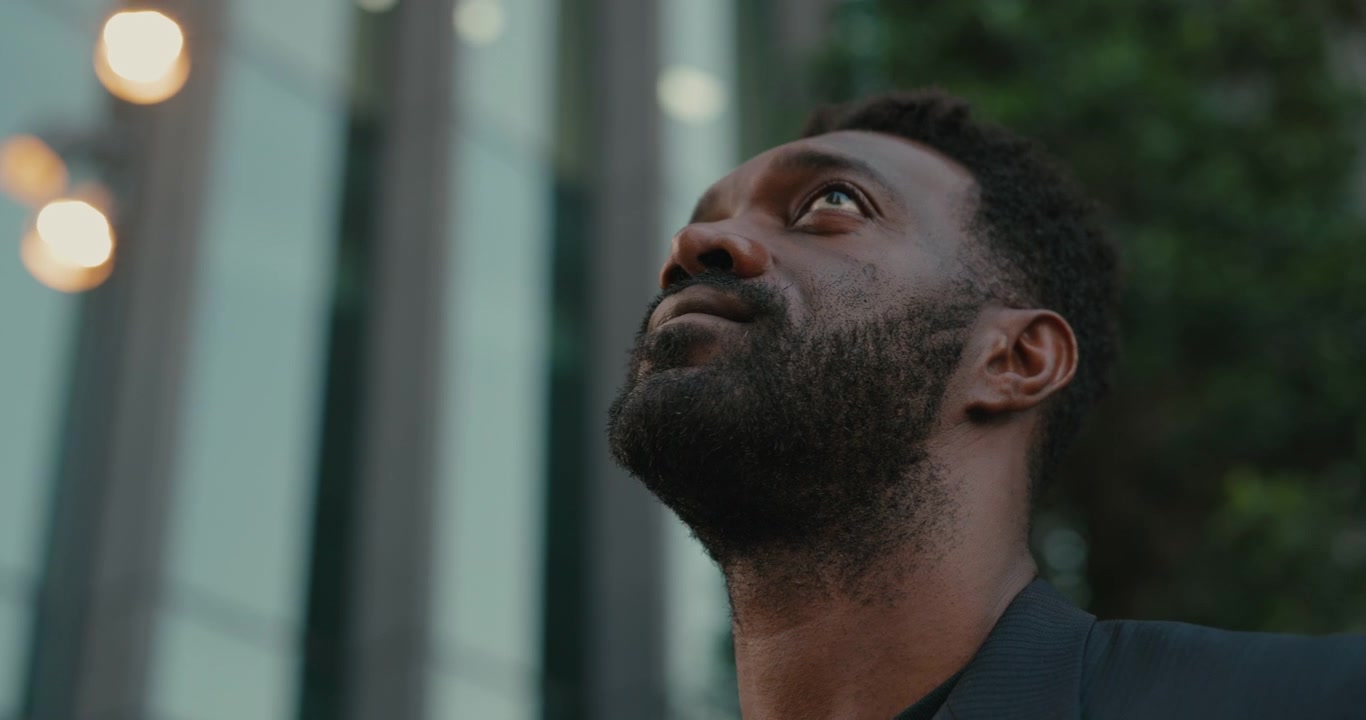 Thoughtful Man Looking Up at Modern Office Building