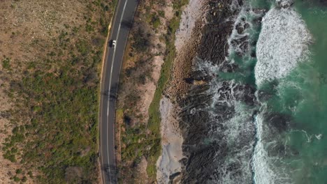 aerial drone view of cars driving next to ocean coastline