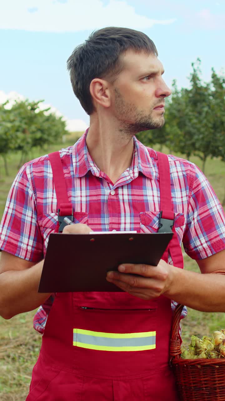 jardinero agrónomo hombre agricultor analizar la calidad de los árboles de avellanas en el jardín haciendo notas en el diario