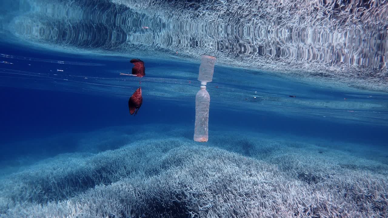 Plastic Bottle Of Water And Dry Leaf Floating On The Crystal Clear Water On The Ocean. - concept of Pollution. - wide to close up shot
