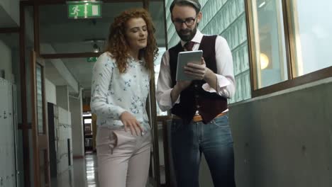 Colleagues-discussing-over-digital-tablet-in-corridor-4k