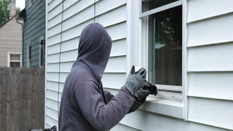 burglar pries open a window with a crowbar and starts to climb into a home