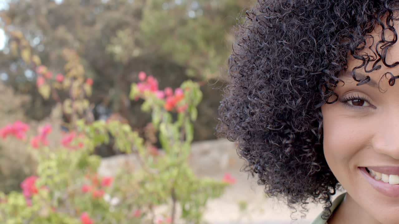 Smiling woman with curly hair enjoying nature in garden with blooming flowers, copy space