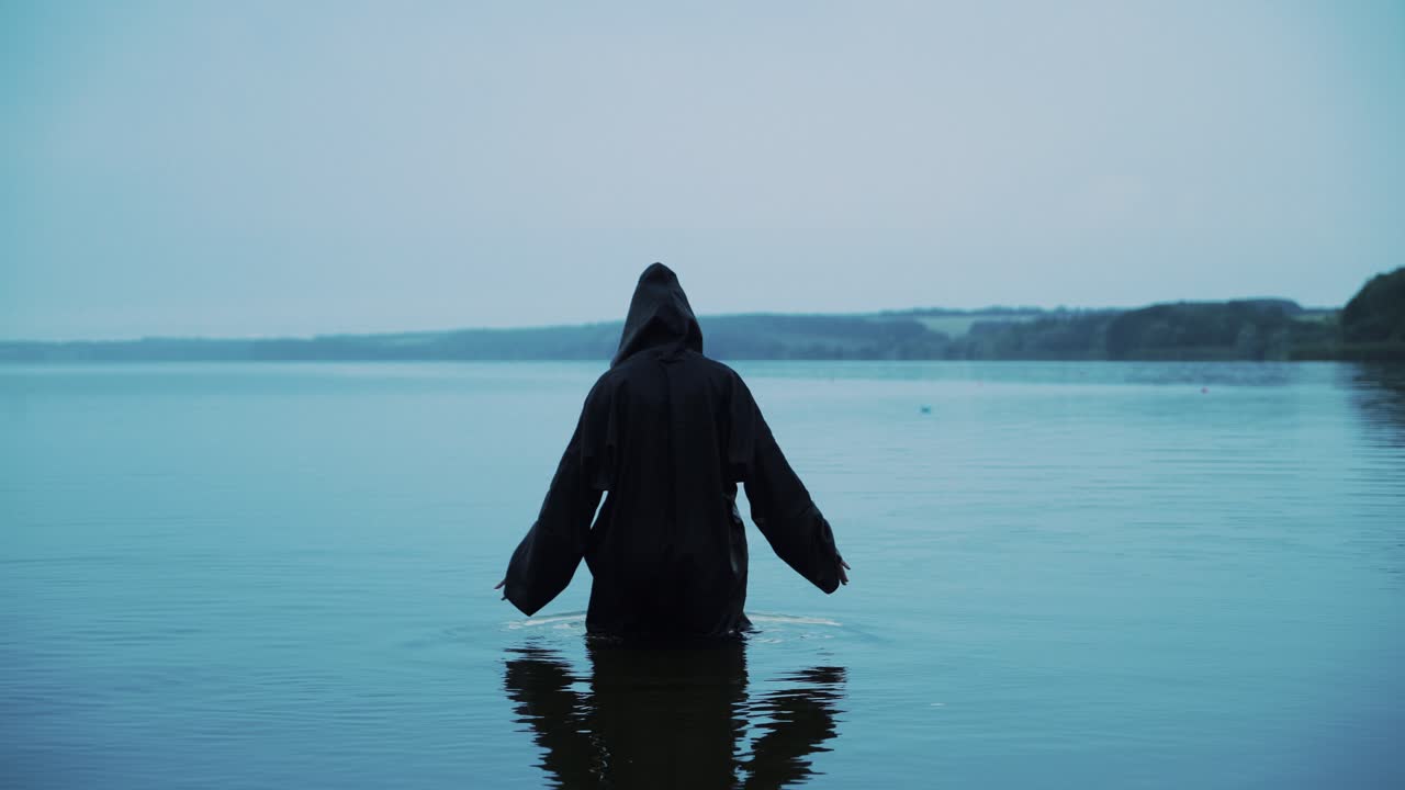 Scary figure in black mantle in the river. Halloween costume