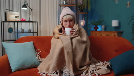 woman sitting on a couch with a cup of coffee and a blanket wrapped around her