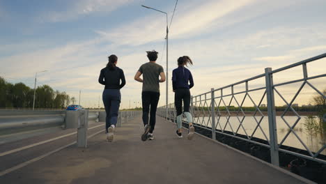 three persons are jogging in outskirts of city in morning rear view of women and man