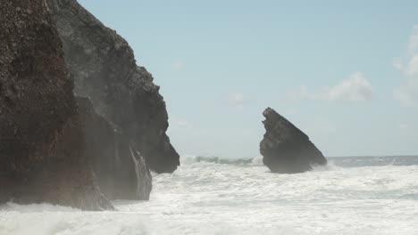 powerful ocean waves come crashing into a rocky cliff side. praia da adraga beach in sintra national park, portugal.
