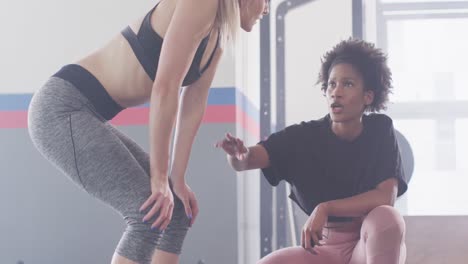 Video-of-diverse-female-fitness-trainer-and-woman-talking-after-working-out-at-a-gym