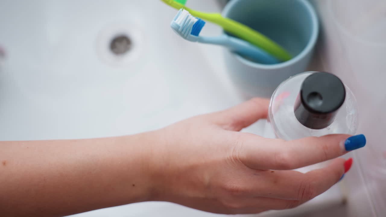 Mujer caucásica muestra artículos de higiene, una mujer presenta elementos básicos de limpieza cerca del lavabo, mujer de ascendencia caucásica sostiene una botella transparente sobre el lavabo mientras está de pie en un baño minimalista