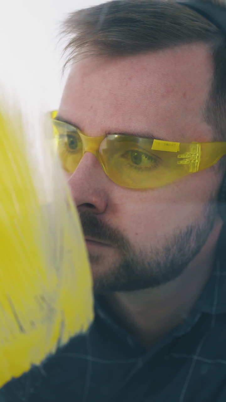 Dolly cam: happy young builder with goggles and headphones paints wall with bright yellow color lying on floor in room