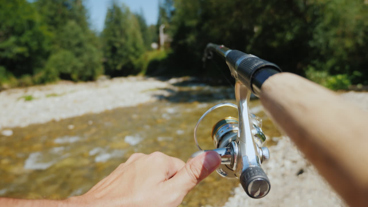 pescando en un pequeño río de montaña en el marco de la mano de un pescador con una caña de pescar