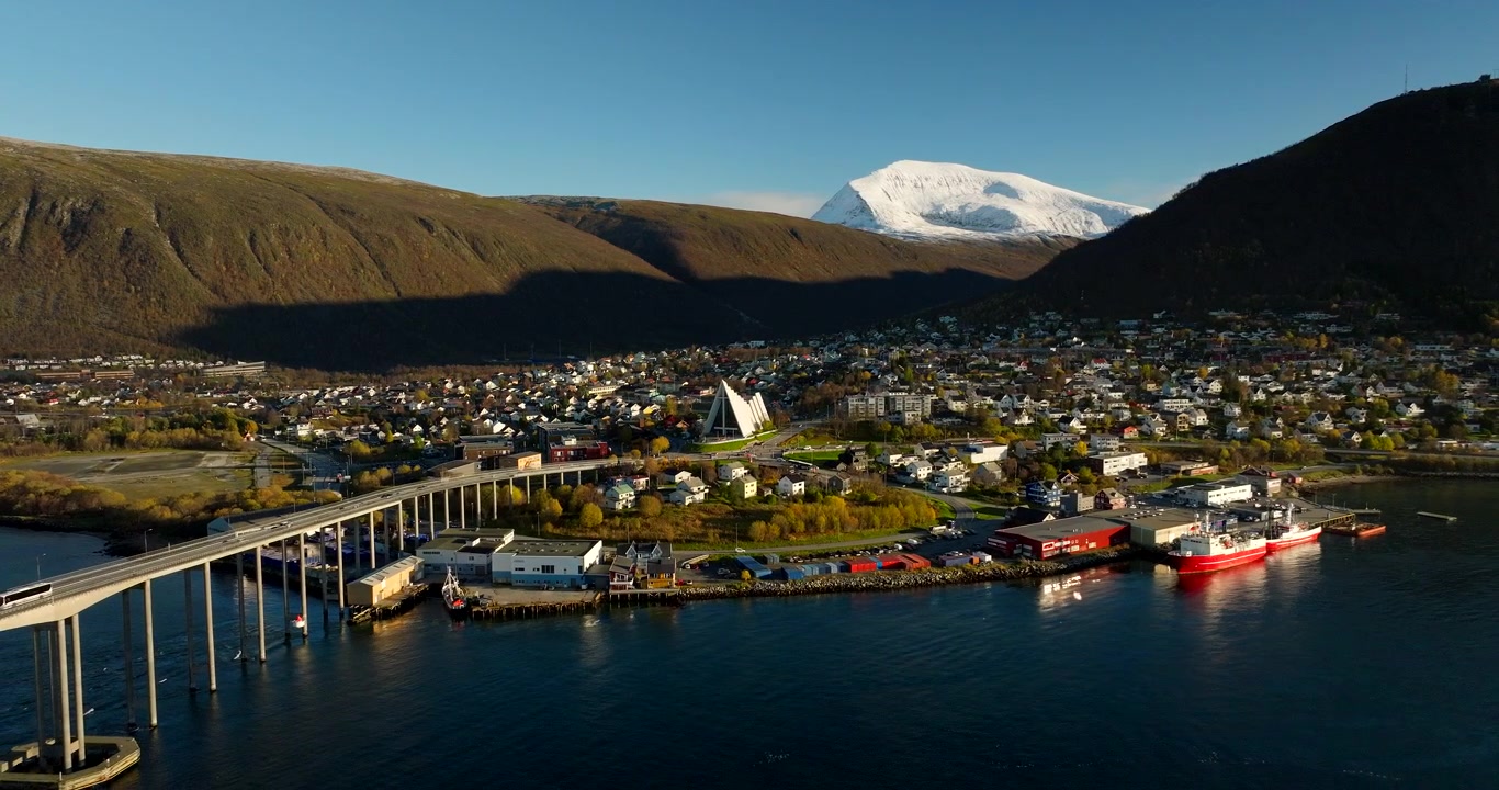 晴れた晩秋のノルウェー、雪を頂いた山々を背景にしたトロムソ市、橋、そして北極圏大聖堂。後方からの空撮。