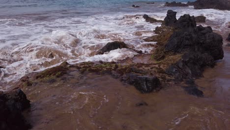 close -up with a slow tilt-up from a large wave rolling up over lava rocks on a maui beach to the ocean horizon