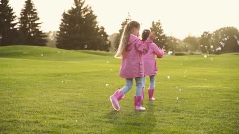 Glückliche-Kleine-Schwestern-In-Identischer-Kleidung,-Die-Im-Park-Seifenblasen-Fangen-1