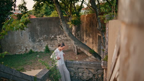 trendy model posing ancient palace in elegant suit. woman leaning stone railings