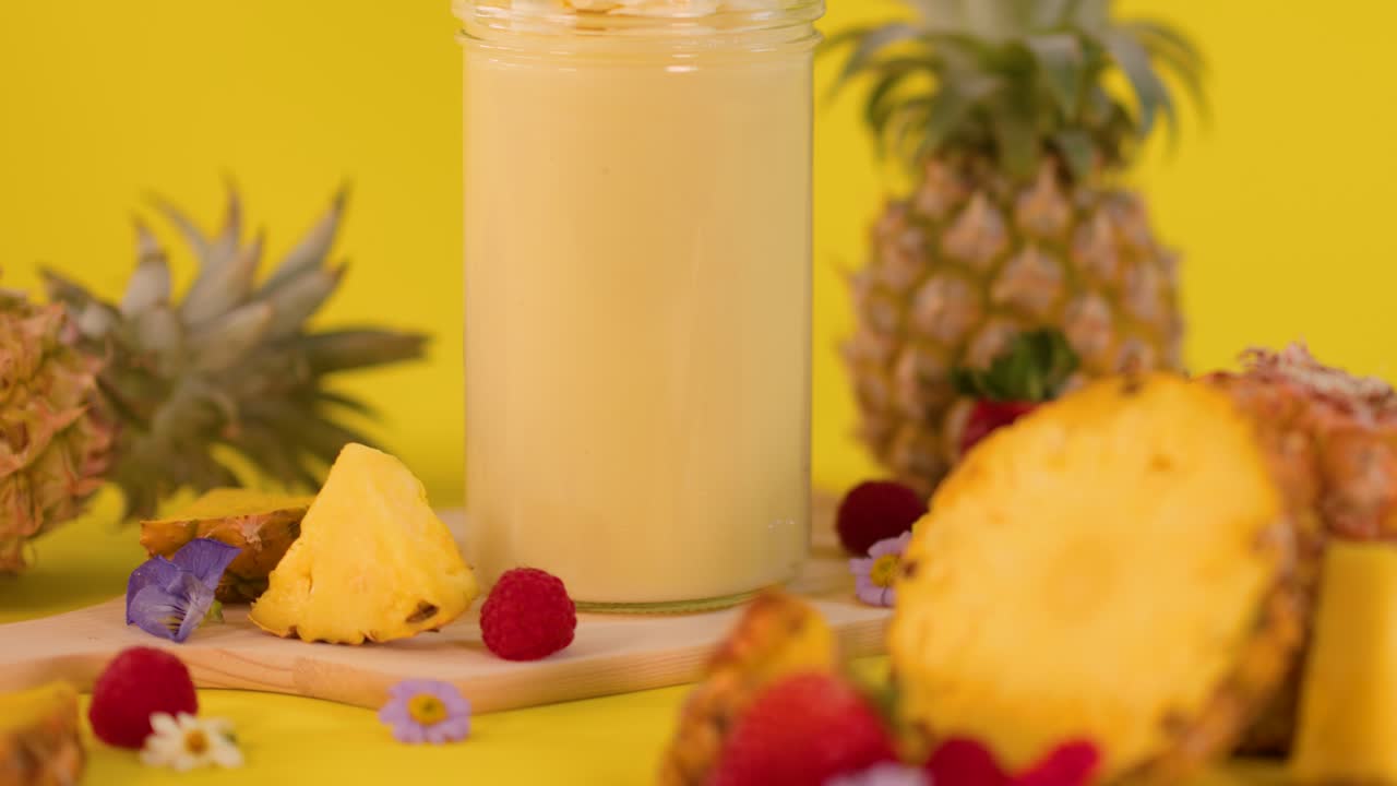 Hand decorates pineapple smoothie topped with whipped cream and sprinkles, vibrant yellow tropical background
