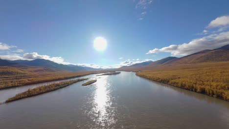 soaring high above vibrant autumn hues, the drone captures the serene flow of the river as golden leaves dance in the breeze, illuminated by the warm glow of the setting sun.