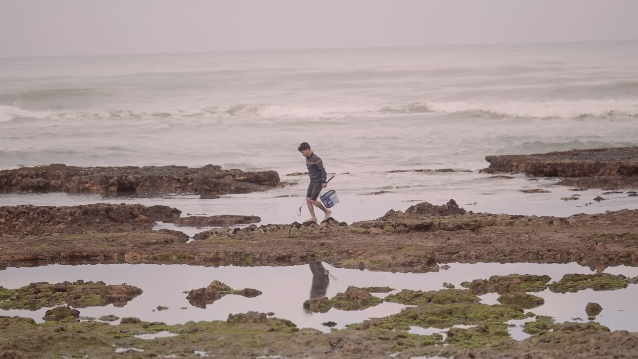 apretado primer plano de un joven pescador caminando en la costa rocosa del océano atlántico en essaouira marruecos