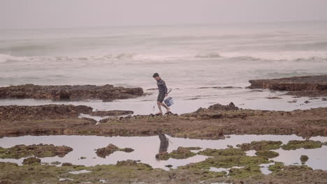 tight close up shot of young fisherman walking on rocky shore of atlantic ocean in essaouira morocco